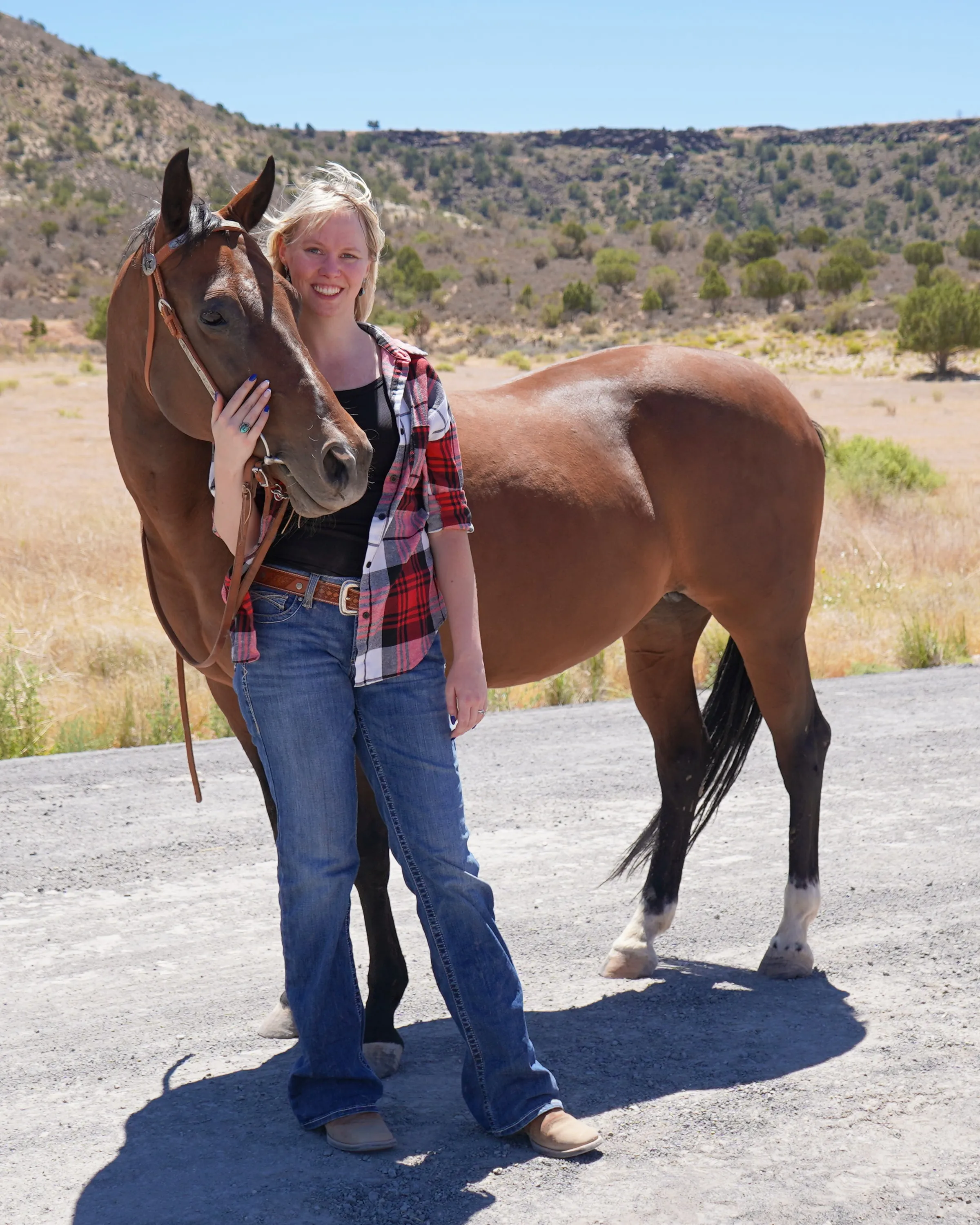 Sydnie Ashbrook standing beside a bay horse in red rock country